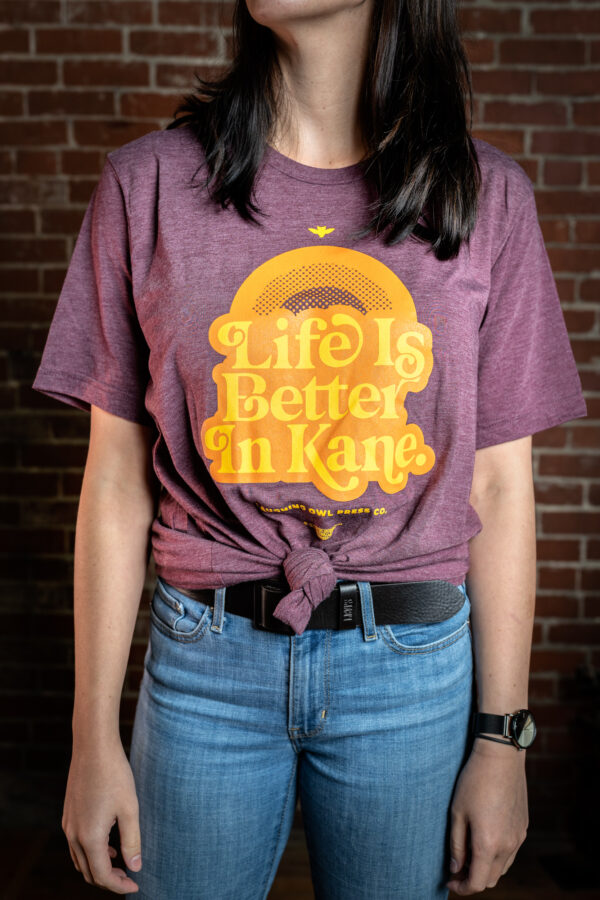 Woman wearing maroon t-shirt that reads life is better in kane in yellow text
